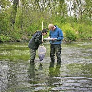 Two volunteers in hip waders conducting water tests