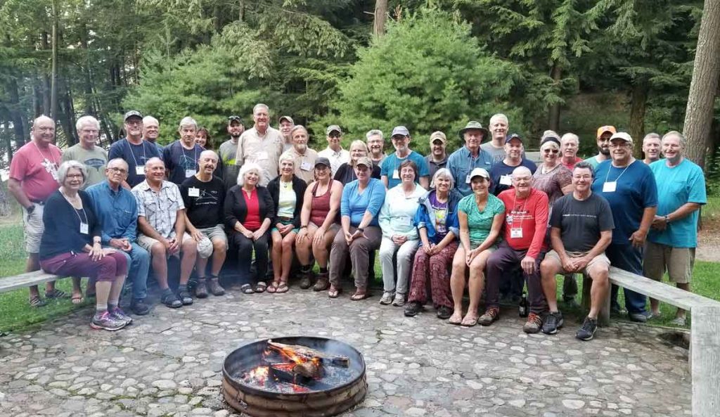 A large group of people sitting and standing in front of a fire pit