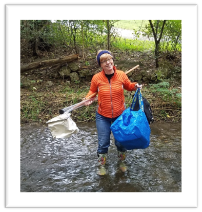 A woman holding some equipment while standing in a stream