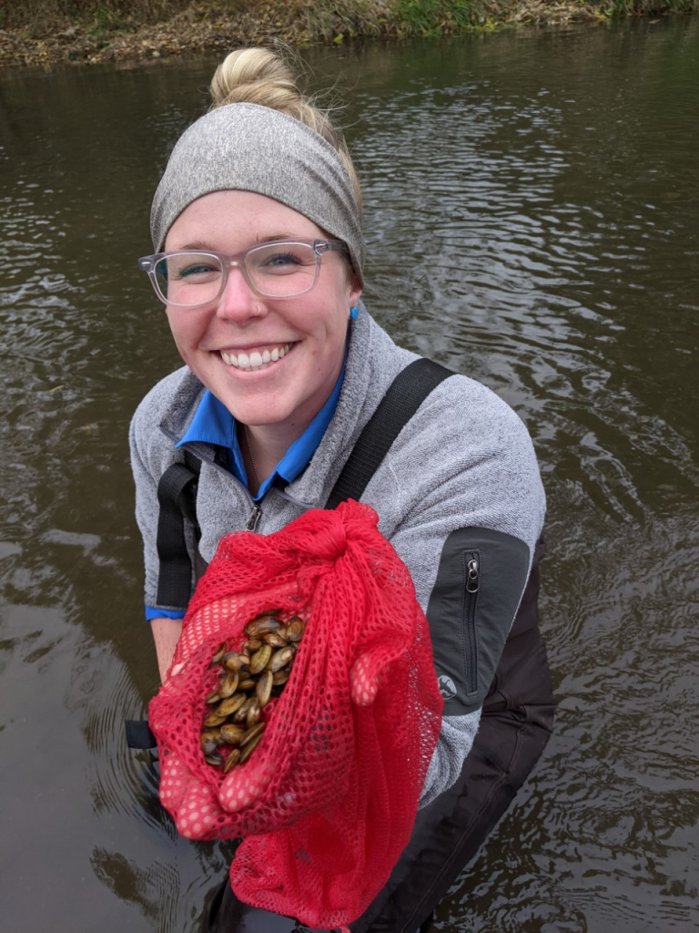 Emily Heald stands in a river and holds up a handful of mussels.
