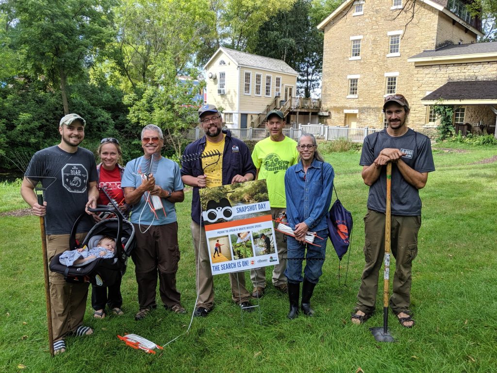 Volunteers stand with garden rakes and a Snapshot Day poster