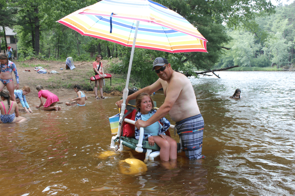 Young girl in beach wheelchair and dad in a lake.