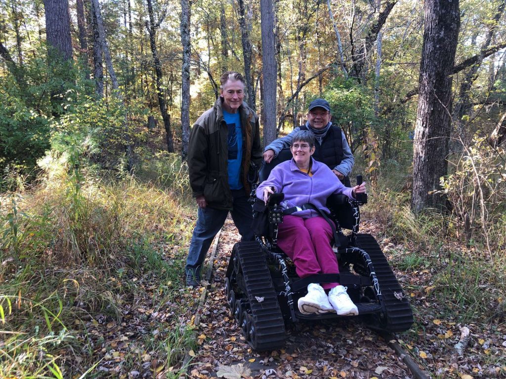 A woman in am all-terrain wheelchair and 2 other visitors explore nature trail.
