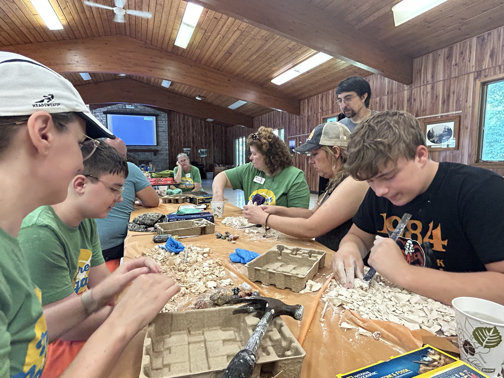 Campers sit around table digging for fossils in rocks