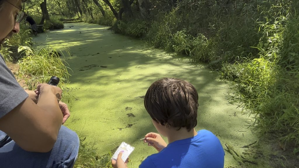 Young man and instructor analyze water sample outside