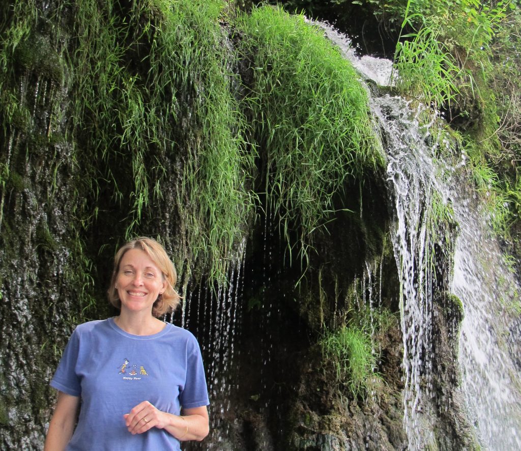 Woman standing next to waterfall on the side of a bluff