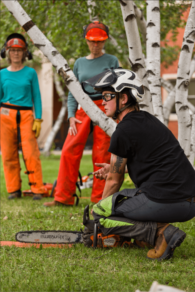 Instructor kneels on the ground explaining chainsaw mechanics