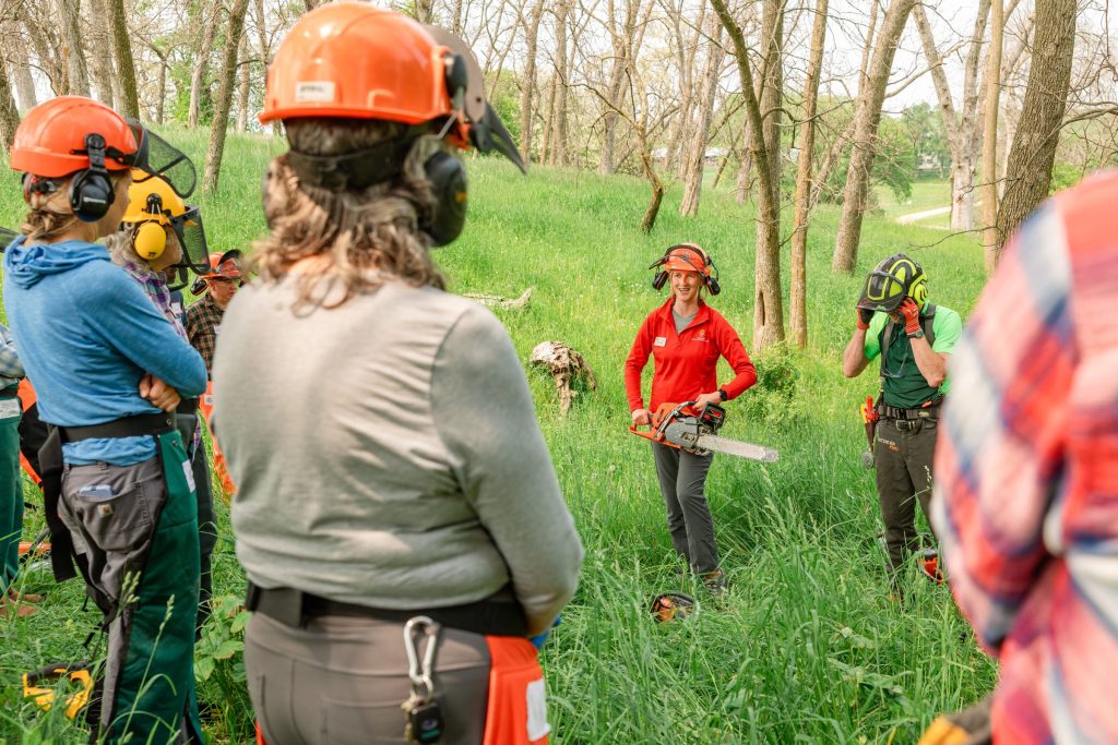 Extension educator standing in a forest with a group of people and a chainsaw in hand