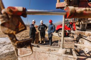Three men standing in front of a well being drilled