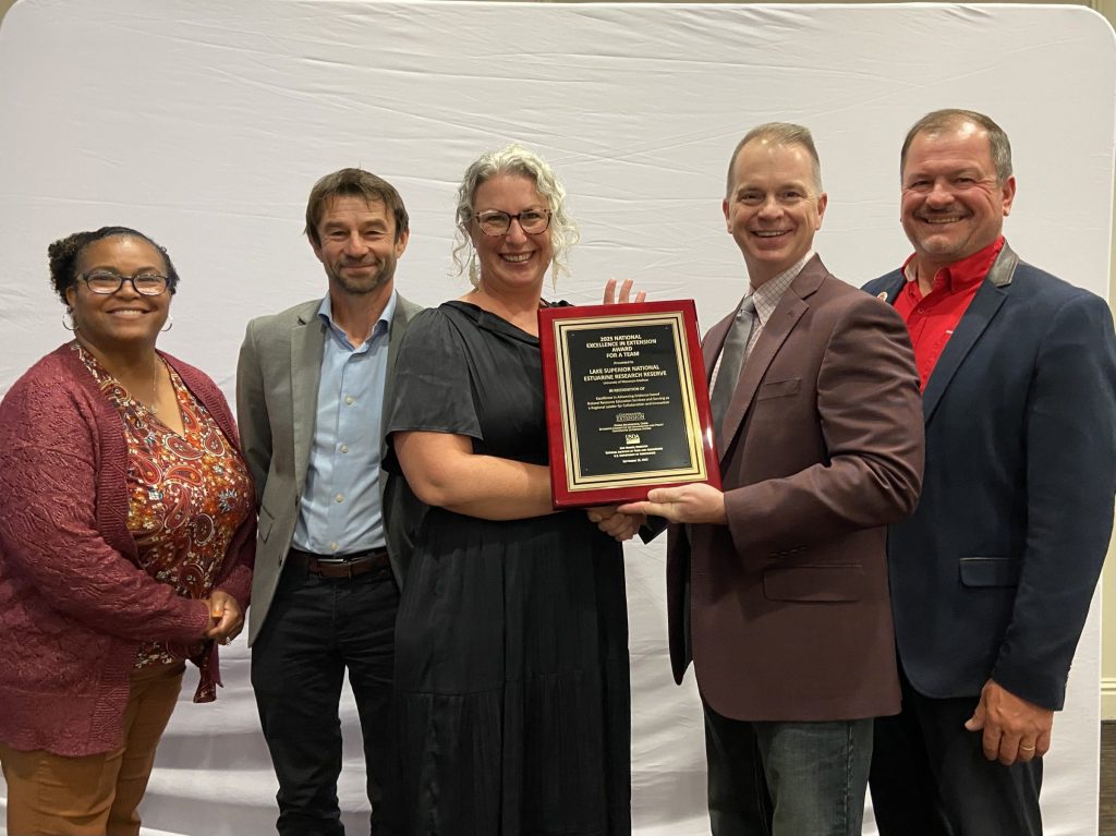 Deanna Erickson, Lake Superior Reserve Director receiving the National Excellence in Extension Team Award. She is standing holding a plague with Extension leadership