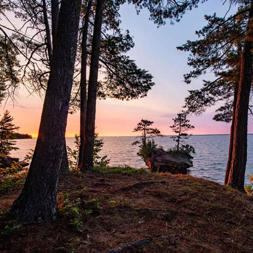 The sun setting over lake superior as seen through a wooded shoreline