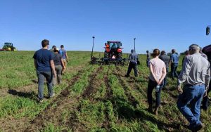 A group of people walking behind a tractor that is planting seeds in a no till field