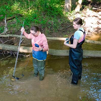 Two women testing water in a small stream