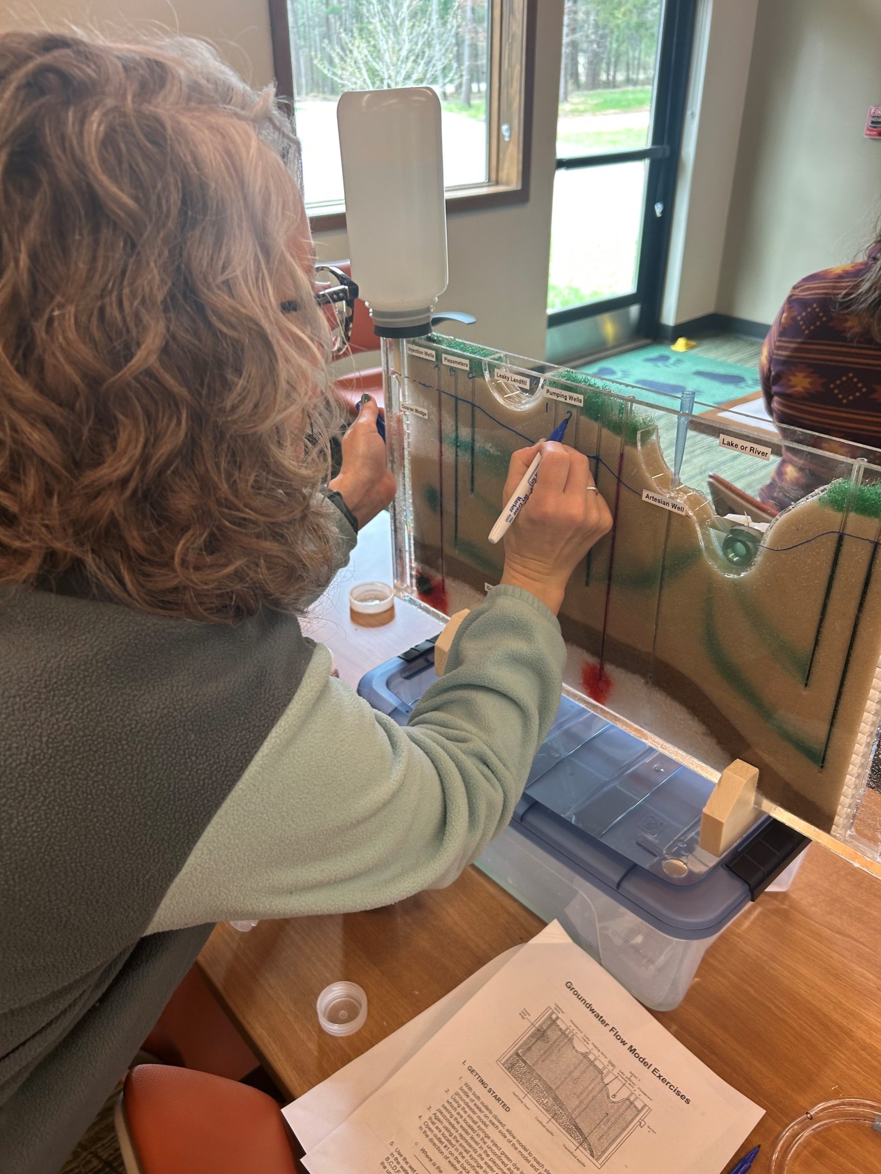 A women leaning over and writing on a sand groundwater model at a Groundwater Model Teacher Workshop
