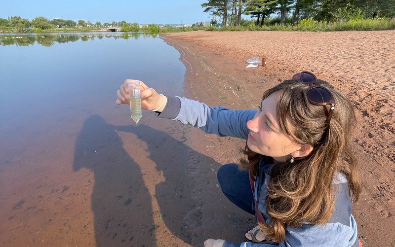 Lake Superior Reserve researcher holding a water sample on a clear day on the shores of Lake Superior