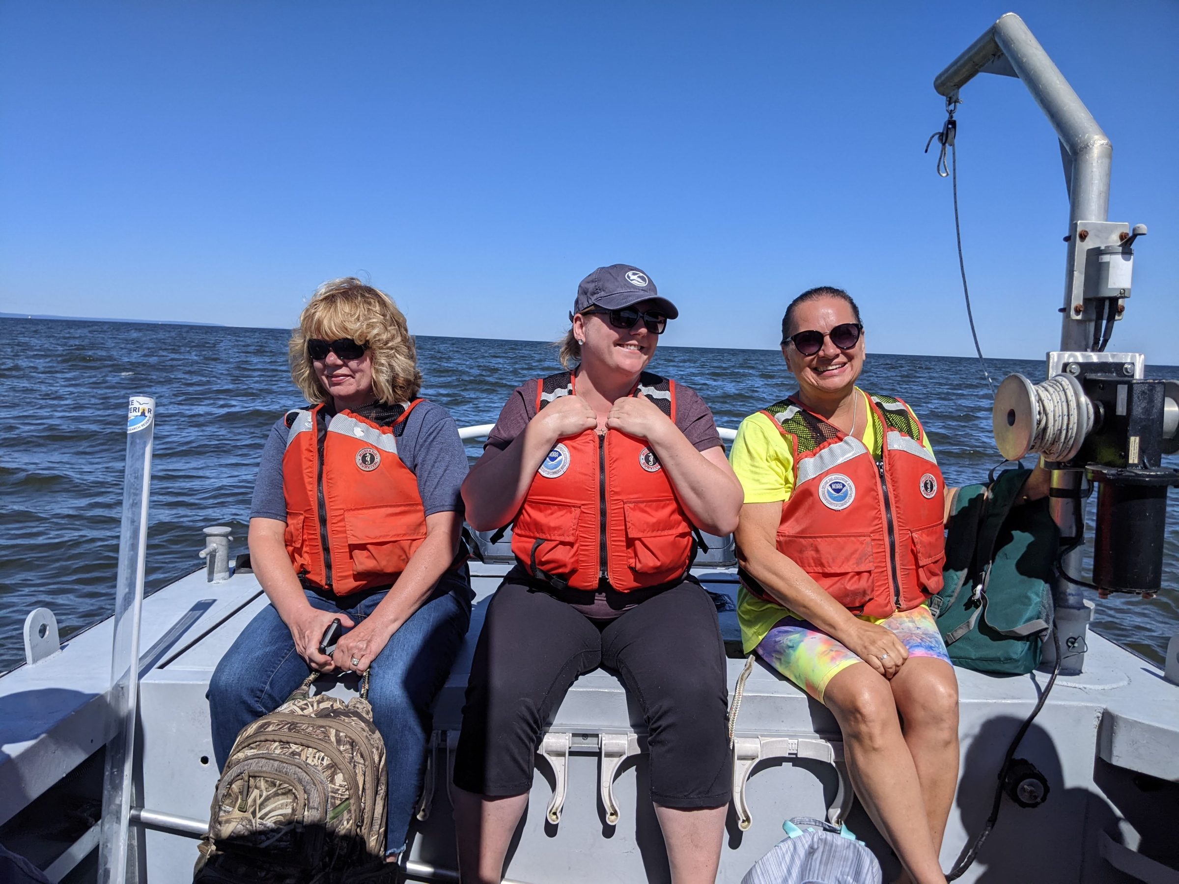 Three teachers in the Rivers2Lake Education program sitting in boat wearing life vests heading out to sample water quality in Lake Superior