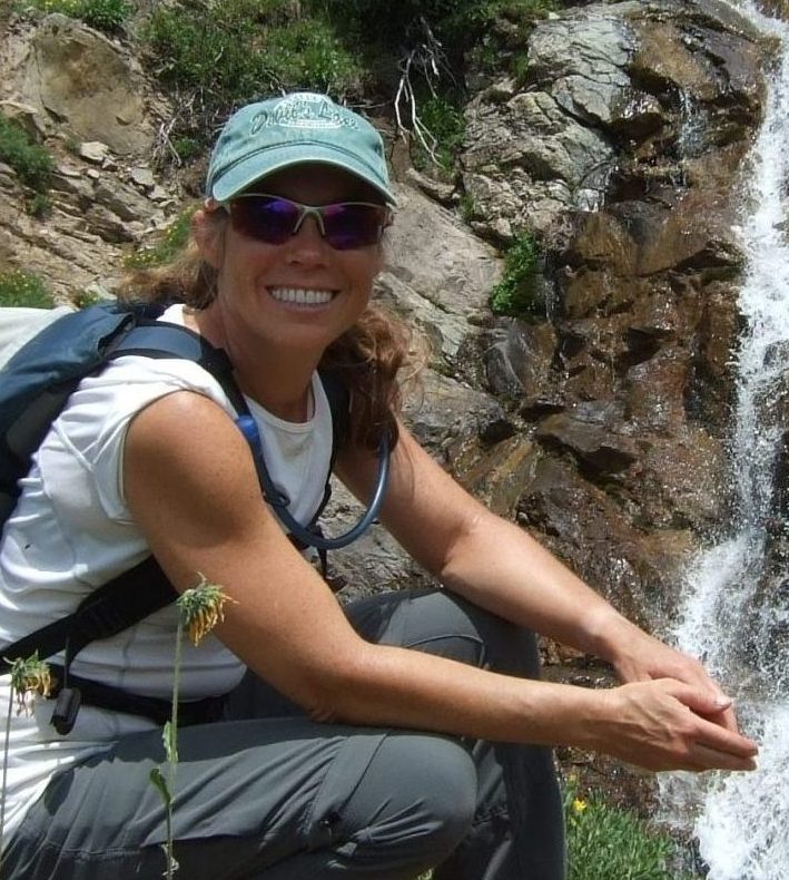 Amy Workman squatting next to a waterfall on a hiking trail