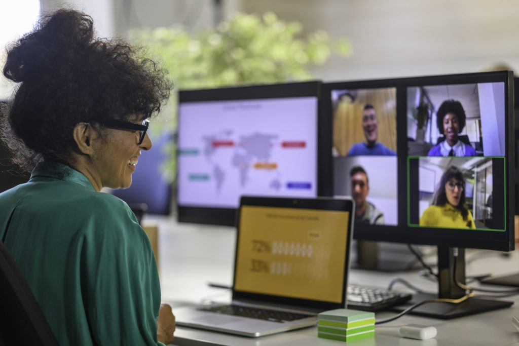 A women sitting at a desk looking at a laptop with 3 screens, one has a map and another has a zoom with 4 people.