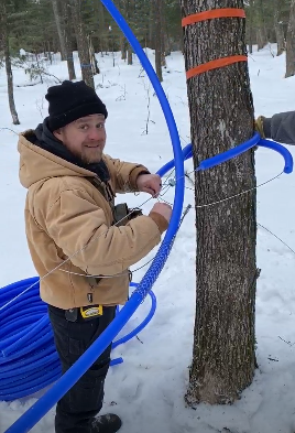 A man in a coat standing in the woods in the snow installing a tubing system.