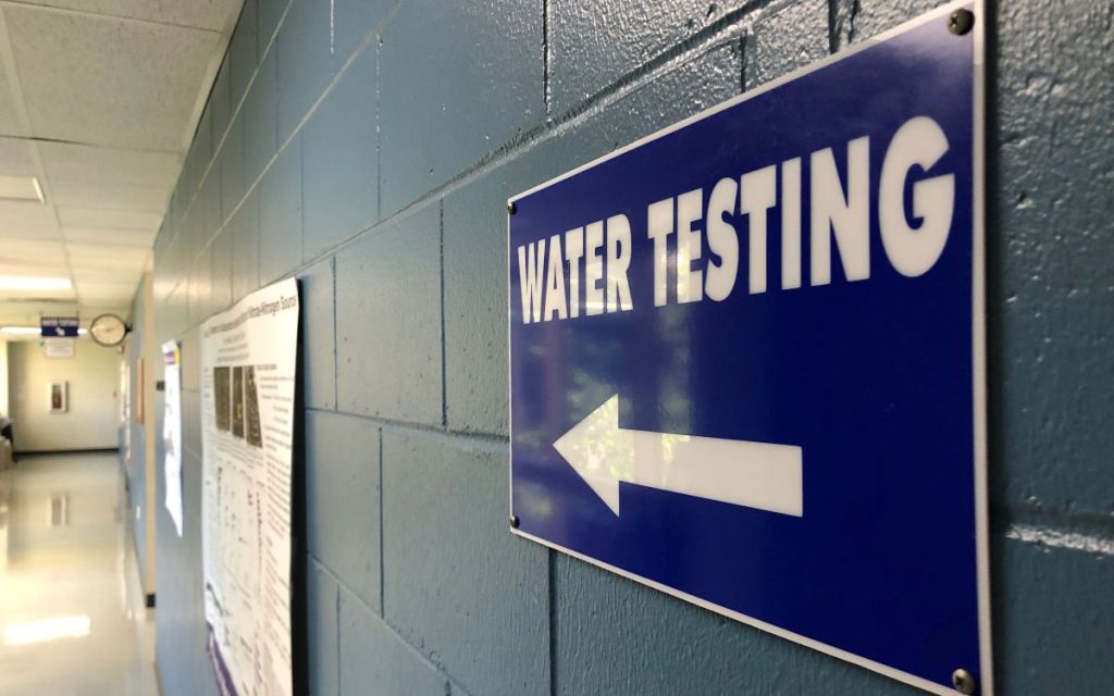A blue sign on a brick hallway wall that says Water Testing