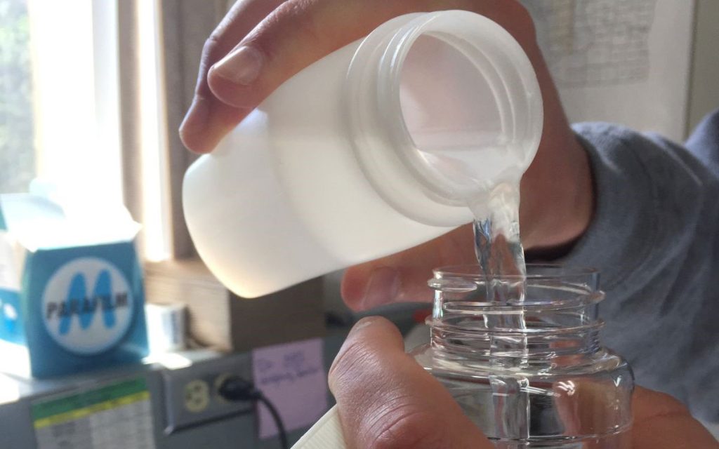 A person pouring water from a white plastic bottle into a clear glass bottle