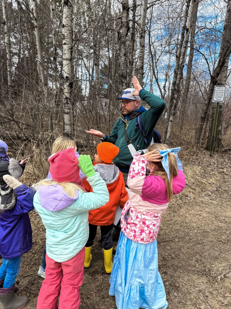 An Extension Educator using his hands to teach a group of elementary age children in the woods.