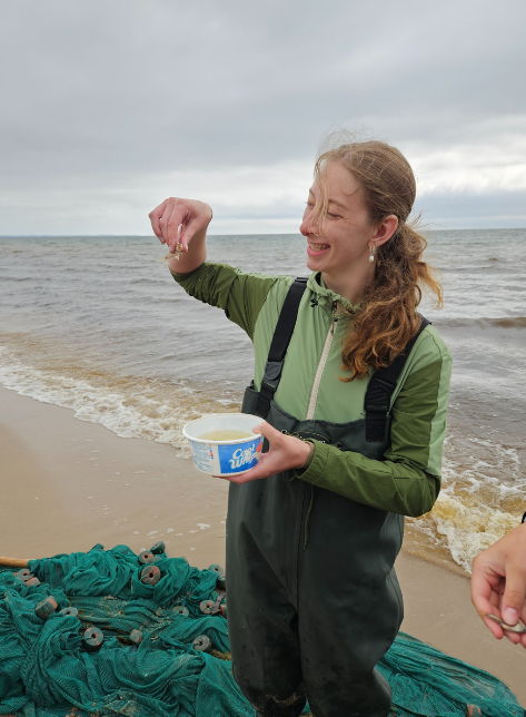 A student holding up a fish on the shores of the Green Bay.