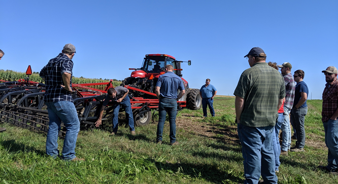 An Extension Educator pointing at farm equipment and explaining strip tillage.