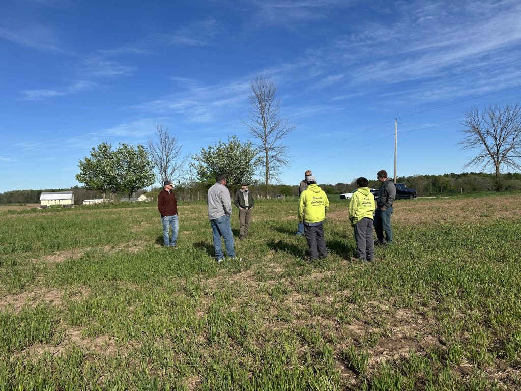 A group of seven farmers standing in a circle in a farm discussing strip tillage.