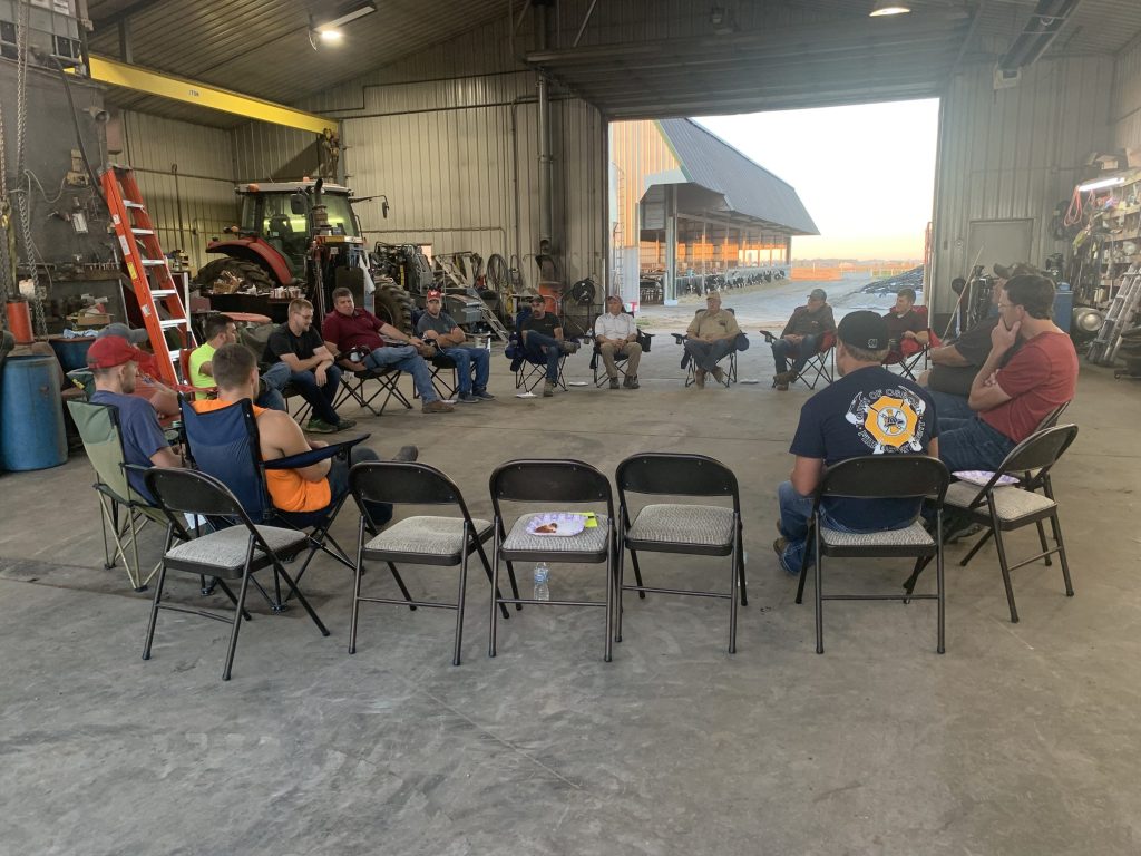 A group of farmers sitting in a circle in a barn