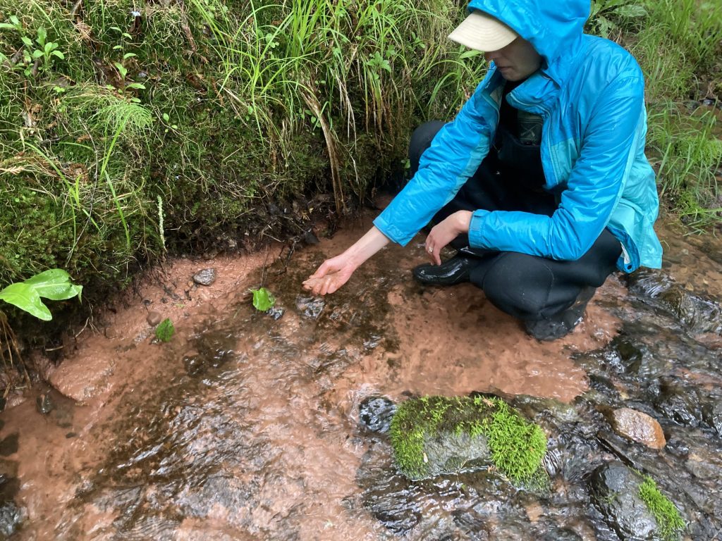 A hydrogeologist in a stream examining sediment.